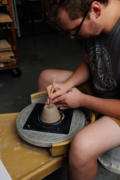 Ceramicist, Chris, sits working at a wheel in Waxman's ceramic studio.