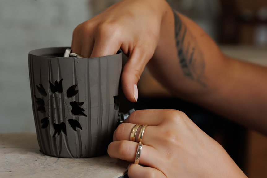 Ceramicist, Mel, cuts a sunflower design into a clay vessel.